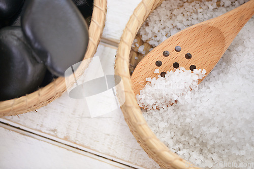 Image of Basket, stone and salt closeup in spa for luxury service in hospitality at hotel on holiday or vacation. Rocks, container and object for wellness treatment on table with detail of pebble or minerals