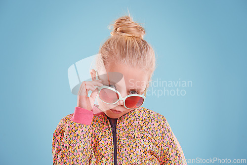 Image of Portrait, fashion and child with sunglasses in studio with trendy, cool and funky outfit with confidence. Stylish, pout and girl kid model with cool style and accessory isolated by blue background.