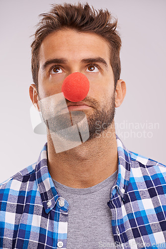 Image of Clown, nose and man thinking with funny, crazy and comedy with idea in a studio. Costume, quirky and looking up with a male person with grey background and comedian ready for a joke with red prop