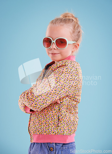 Image of Child, portrait and fashion with sunglasses in studio for trendy, cool and funky style with confidence. Cute girl, smile and happy in blue background, young kid and retro clothes with glasses