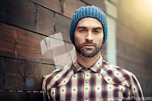 Image of Portrait, confident and man on wood wall background outdoor in casual clothes, outfit or apparel. Face, serious and stylish person in beanie, shirt and trendy fashion for profile picture in Spain