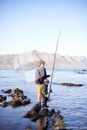 Image of Father, fishing rod and young boy on rocks, teaching and bonding for activity by ocean. Sea, teach and learn to fish for childhood development, winter and hobby together while on countryside vacation