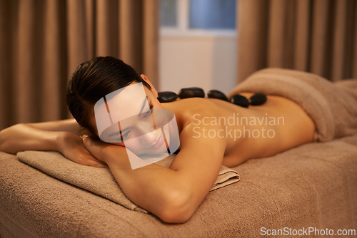 Image of Woman, relax and hot stone massage at spa for self care, organic body health and wellness. Bed, towel and zen female person with rock therapy for stress relief, detox and healing at luxury hotel