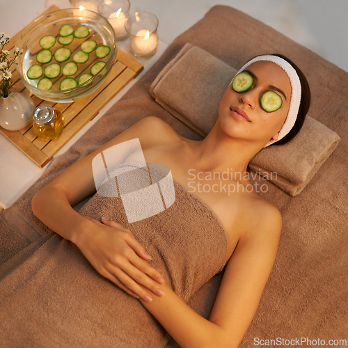 Image of Top view, skincare and woman with cucumber on face at massage table in spa for peace, relax or wellness. Facial, above or person with vegetable on eyes for natural beauty or healthy organic treatment