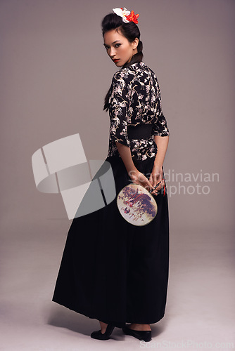 Image of Asian woman, fashion and fan in studio on brown background in confidence, traditional style and elegant. Portrait, Japanese and female person with designer, culture and outfit for heritage.