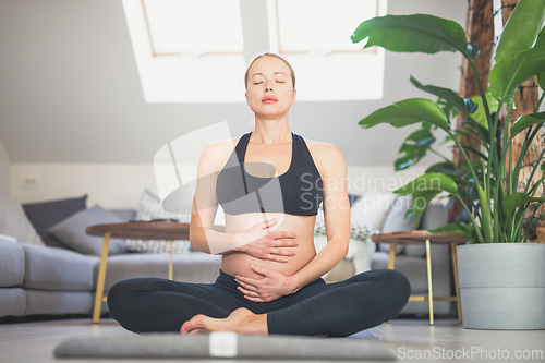 Image of Young beautiful pregnant woman training yoga, caressing her belly. Young happy expectant relaxing, thinking about her baby and enjoying her future life. Motherhood, pregnancy, yoga concept.