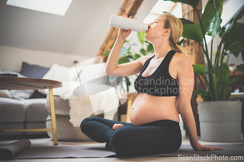 Image of Young happy and cheerful beautiful pregnant woman taking a break, hydrating, drinking water from the botle after home well being workout progrem.