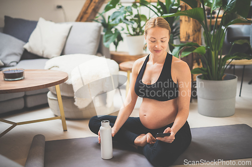 Image of Young happy and cheerful beautiful pregnant woman chating to family and friends on mobile phone while staying fit, sporty and active on her maternity leave. Pregnancy, yoga concept