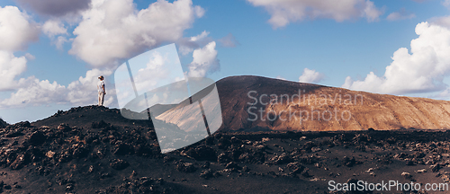 Image of Woman rising hands up in the sky, enjoying amazing views of volcanic landscape in Timanfaya national park on Lanzarote, Spain. Freedom and travel adventure concept.