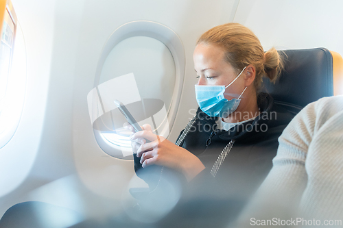 Image of A young woman wearing face mask, using smart phone while traveling on airplane. New normal travel after covid-19 pandemic concept.