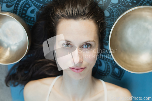 Image of Yoga concept, meditation and sound therapy. Portrait of beautiful young caucasian woman surrounded by copper tibetan singing bowls and instruments