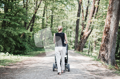 Image of Rear view of casually dressed mother walking with baby stroller in Koseski bajer city park in Ljubljana, Slovenia. Family, child and parenthood concept.