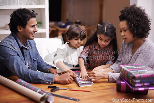 Image of Parents, kids and table with wrapping gift or presents for Christmas season with smile, support and bonding. Home, family and happy together in living room for child development, growth and memories