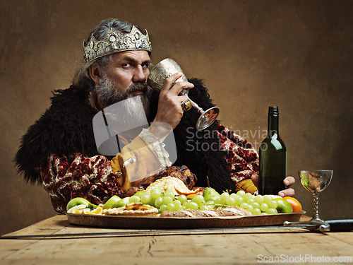 Image of King, confident and feast at table with wine glass as royalty in studio on brown background for tradition, culture and meal. Portrait, monarch and leader with eating buffet or supper with confidence