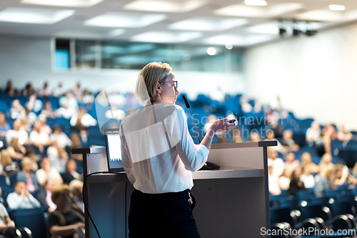 Image of Female speaker giving a talk on corporate business conference. Unrecognizable people in audience at conference hall. Business and Entrepreneurship event.