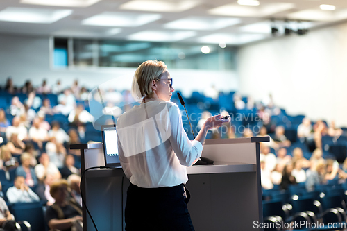Image of Female speaker giving a talk on corporate business conference. Unrecognizable people in audience at conference hall. Business and Entrepreneurship event.