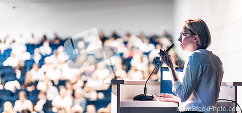 Image of Female speaker giving a talk on corporate business conference. Unrecognizable people in audience at conference hall. Business and Entrepreneurship event.