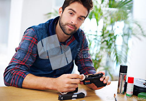 Image of Portrait, cleaning and man with gun at table for safety, self defense and confident handgun assembly. Process, equipment and person with firearm maintenance, cloth and wiping dust, dirt and tools