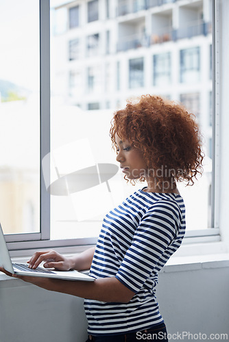 Image of Office, window and black woman typing on laptop with research or online communication on email. Creative, employee and working with computer to scroll information or news on internet for business