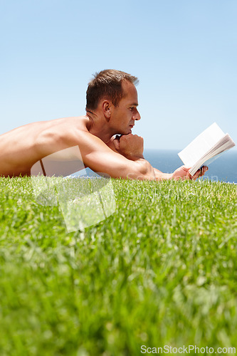 Image of Man, book and reading on lawn in summer by ocean with knowledge, relax and information on vacation. Person, thinking and novel on grass with ideas, topless and outdoor for holiday by sea in Naples