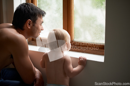 Image of Rain, window and father with baby in a house for bonding, playing or having fun in their home together. Water, glass or dad with curious kid watching storm, weather or raindrops for learning or games