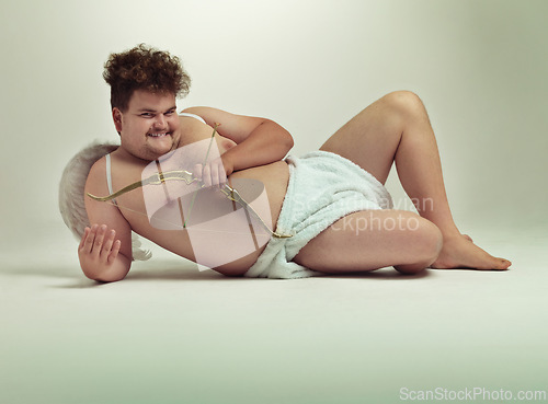 Image of Humor, cupid and portrait of man with costume in studio for wings, bow and arrow on gray background. Fantasy, love and plus size male model lying down for role play, creative dress up or cosplay