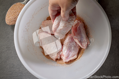 Image of cook put fresh raw chicken wings in bowl of spices