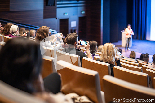 Image of Speaker giving a talk in conference hall at business event. Rear view of unrecognizable people in audience at the conference hall. Business and entrepreneurship concept.