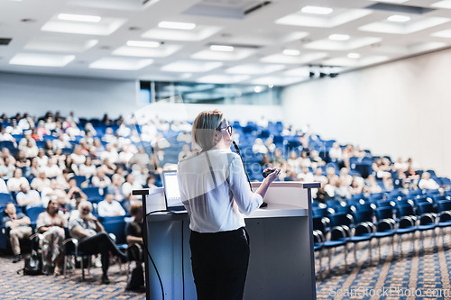 Image of Female speaker giving a talk on corporate business conference. Unrecognizable people in audience at conference hall. Business and Entrepreneurship event.