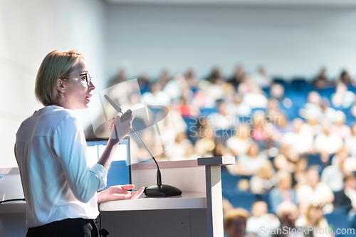 Image of Female speaker giving a talk on corporate business conference. Unrecognizable people in audience at conference hall. Business and Entrepreneurship event.