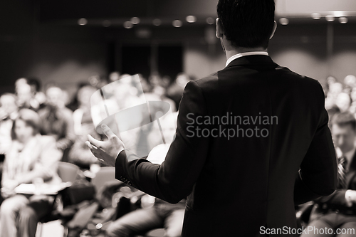 Image of Speaker giving a talk in conference hall at business meeting event. Rear view of unrecognizable people in audience at the conference hall.