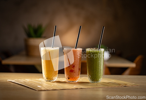 Image of Three different refreshing smoothies with black straws sitting o