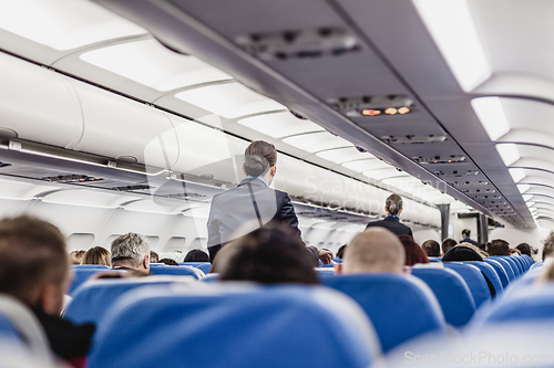 Image of Stewardess walking the aisle of commercial airplane.