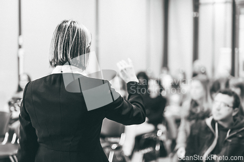 Image of Female speaker giving a talk on corporate business conference. Unrecognizable people in audience at conference hall. Business and Entrepreneurship event. Black and white.