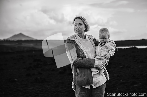Image of Mother enjoying winter vacations playing with his infant baby boy son on black sandy volcanic beach of Janubio on Lanzarote island, Spain on windy overcast day. Family travel vacations concept.