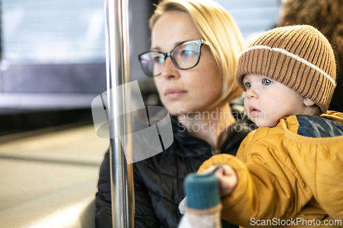 Image of Mother carries her child while standing and holding on to the bus. Mom holding her infant baby boy in her arms while riding in a public transportation. Cute toddler boy traveling with his mother.