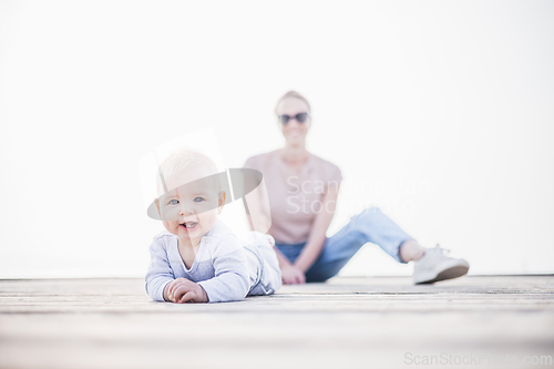 Image of Happy family. Young mother playing with her baby boy infant oudoors on sunny autumn day. Portrait of mom and little son on wooden platform by lake. Positive human emotions, feelings, joy.