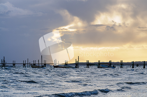 Image of Serene Sunset Over Calm Waters With Fishing Boats and Stilted Do