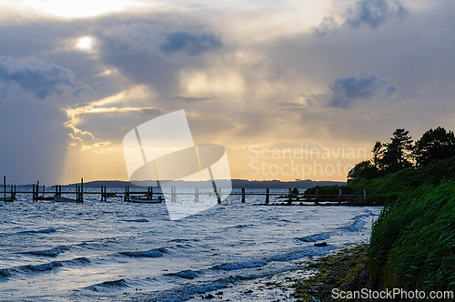 Image of Dramatic Sunset Over Calm Waters With Pier Amidst Gathering Stor