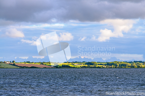 Image of Tranquil Waters Reflecting Lush Green Hills Under Dramatic Cloud