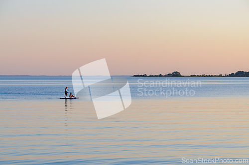 Image of Two Paddleboarders Glide Across Tranquil Waters at Dusk Under So
