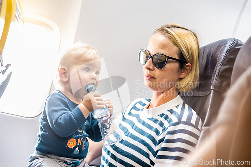 Image of Mom and child flying by plane. Mother holding and playing with her infant baby boy child in her lap during economy comercial flight. Concept photo of air travel with baby. Real people.
