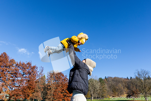 Image of More, more,...mum, that's fun. Happy young mother throws her cute little baby boy up in the air. Mother's Day, Mather and her son baby boy playing and hugging outdoors in nature in fall.