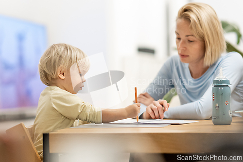 Image of Caring young Caucasian mother and small son drawing painting in notebook at home together. Loving mom or nanny having fun learning and playing with her little 1,5 year old infant baby boy child.