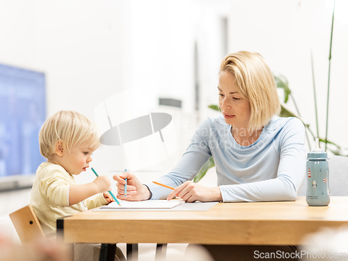 Image of Caring young Caucasian mother and small son drawing painting in notebook at home together. Loving mom or nanny having fun learning and playing with her little 1,5 year old infant baby boy child.