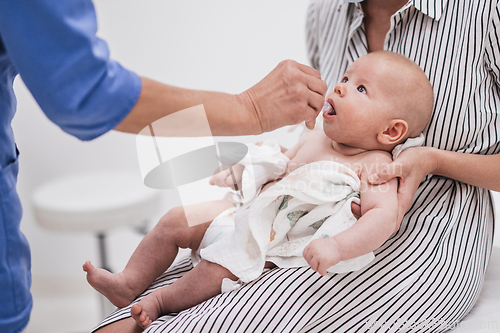 Image of Pediatrician administring oral vaccination against rotavirus infection to little baby in presence of his mother. Children health care and disease prevention