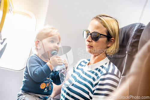 Image of Mom and child flying by plane. Mother holding and playing with her infant baby boy child in her lap during economy comercial flight. Concept photo of air travel with baby. Real people.