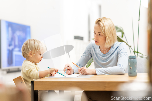 Image of Caring young Caucasian mother and small son drawing painting in notebook at home together. Loving mom or nanny having fun learning and playing with her little 1,5 year old infant baby boy child.