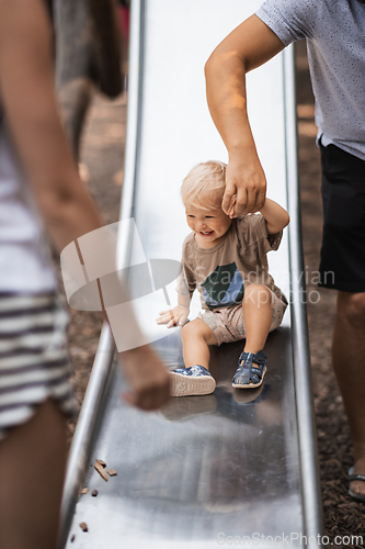 Image of Parent hand holding little infant baby boy child while sliding on urban playground on a sunny summer day. Family joy and happiness concept