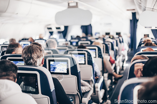 Image of Interior of airplane with passengers on seats and stewardess in uniform walking the aisle, serving people. Commercial economy flight service concept.